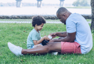 Dad showing son baseball glove while sitting on lawn in park